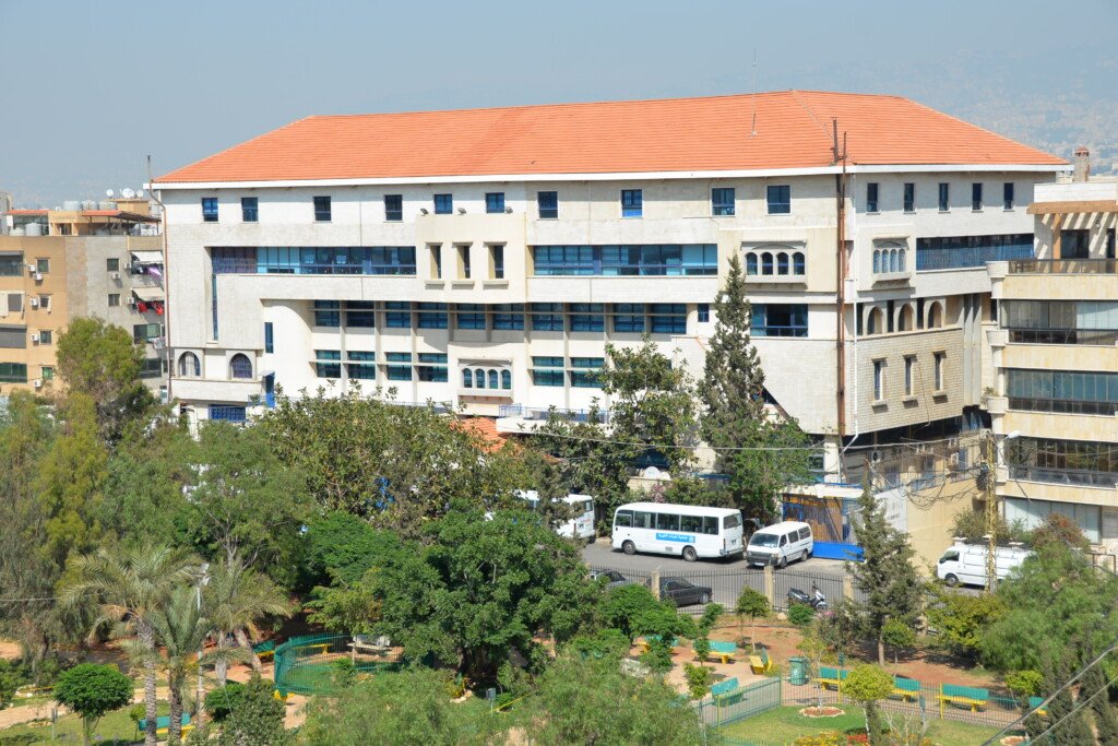 مبنى مؤسسة الهادي بسقفه القرميدي على طريق المطار في بيروت وحافلات مدرسية عند مدخله | Al-Hadi Institution building with its red-tiled roof on Airport Road, Beirut, with school buses at the entrance