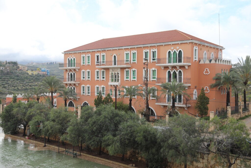 مبنى مبرة السيدة مريم (ع) البرتقالي بسقفه القرميدي وأشجار النخيل حوله | The orange building of Al-Sayyida Mariam Mabarra with its tiled roof and palm trees
